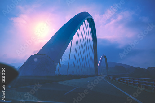 View of the bridge over the Navia river through the windscreen. Navia, Asturias, Spain. Beautiful evening landscape with highway, bridge and dramatic sky