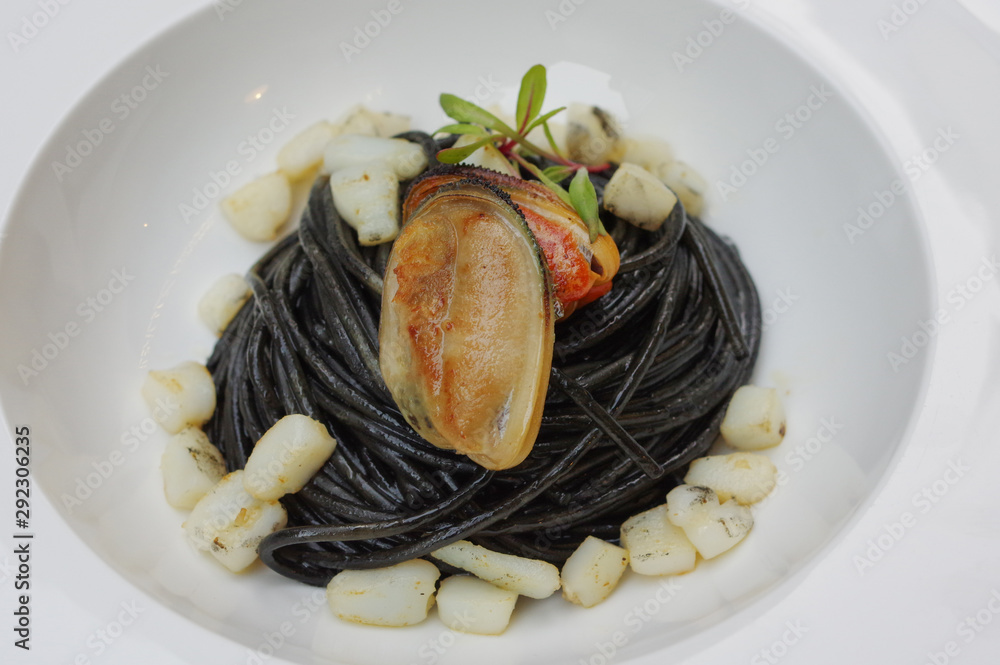 Squid ink black pasta with mussel meat in white bowl plate at Italian cuisine restaurant Squid ink black pasta with mussel meat in white bowl plate at Italian cuisine restaurant
