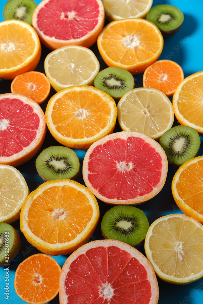 Fototapeta premium Fresh summer fruits on blue background. Healthy food concept. Flat lay. Tropical summer mix grapefruit, orange, mandarin, kiwi, lemon