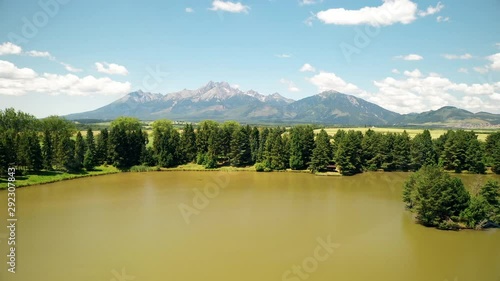 Aerial footage of a lake with a small island with spruce trees and mountain range in the background. High Tatras and Belianske Tatras. Spisska Bela, Slovakia. photo