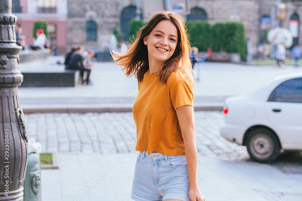 Young exited middle age brunette female student traveler in orange t-shirt and blue denim shorts Young exited middle age brunette female student traveler in orange t-shirt and blue denim shorts