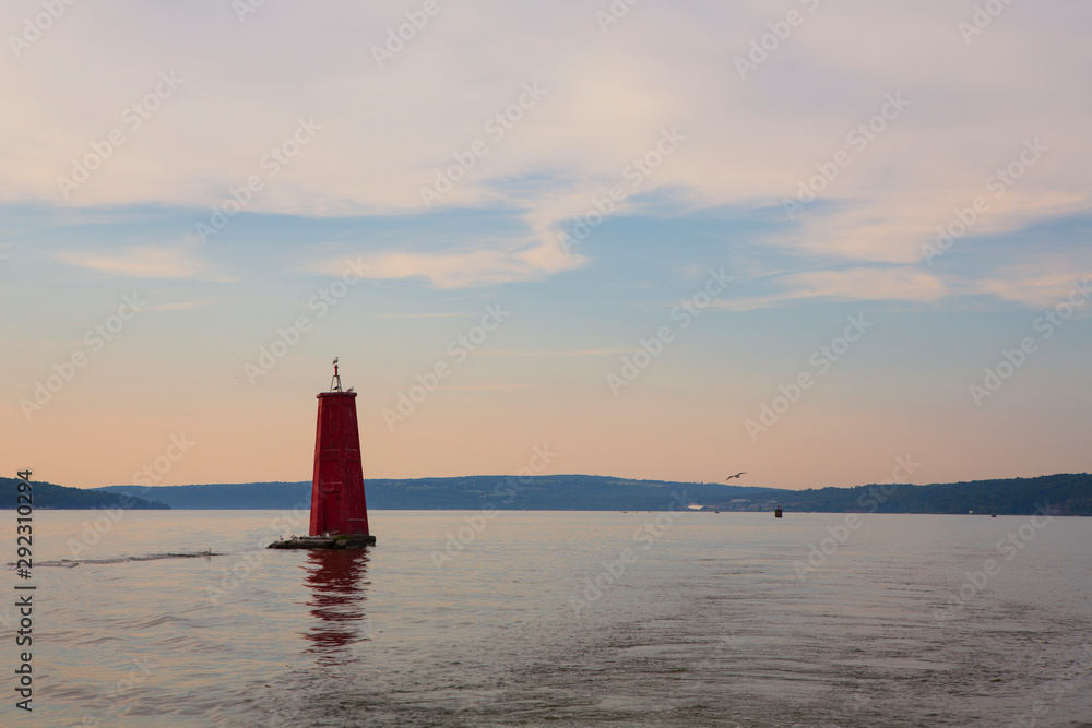 A large red buoy marks the entrance of Cayuga Inlet off Cayuga Lake, in Ithaca, New York State in the Finger Lakes Region during a calm sunset. 