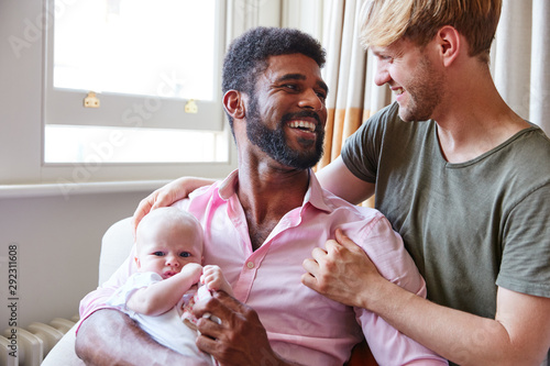 Loving Male Same Sex Couple Cuddling Baby Daughter On Sofa At Home Together photo