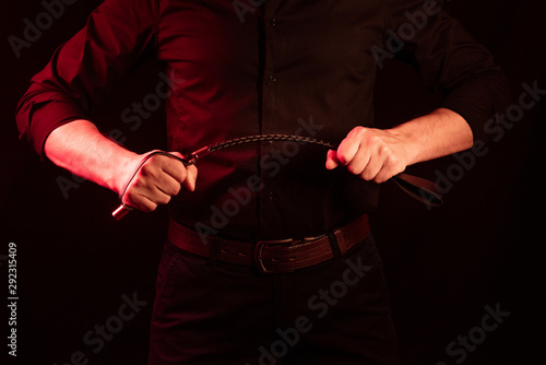 male hand holding black leather whip. flogger