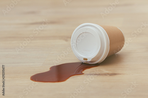 Spilled liquid on the floor. Paper coffee cup with plastic lid. Garbage. Sticky surface. Need cleaning.