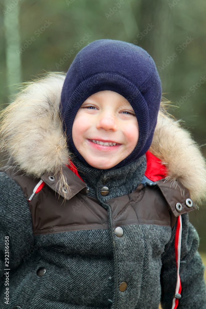 happy smiling boy in warm clothes and hat covering his neck from cold wind llooking at camera in autumn outdoor happy smiling boy in warm clothes and hat covering his neck from cold wind llooking at camera in autumn outdoor