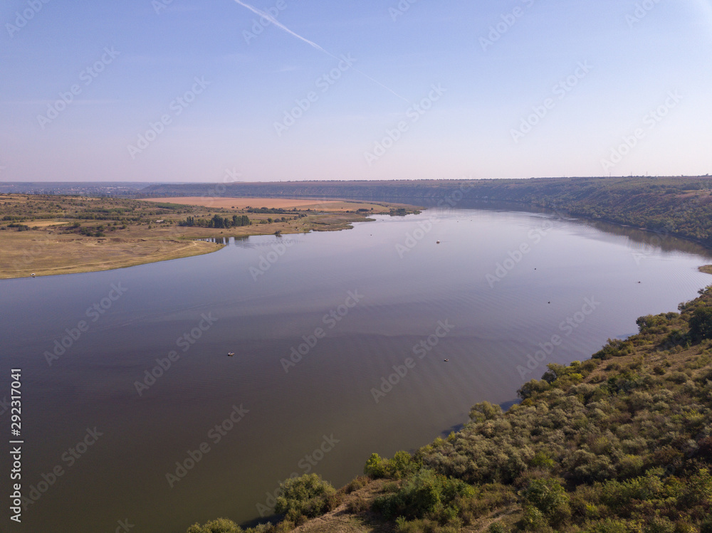 Top view of Dnestr (Dniester) river in autumn. River surrounds yellow field and green forest. Moldova republic of.