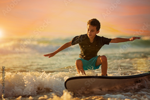 Canvas Print Carefree boy surfing at wave at colourful sunset
