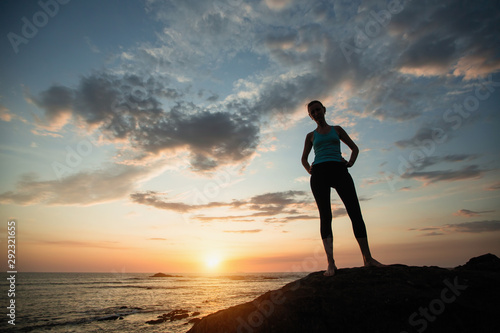 Young woman doing exercises on the ocean during sunset.