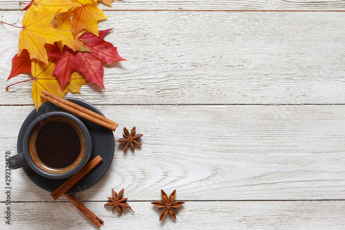 Grey cup of coffee, cinnamon, anise, red and yellow maple leaves on white wooden table. Autumn background concept. Fall menu, expresso, coffee shop, break, copy space, page