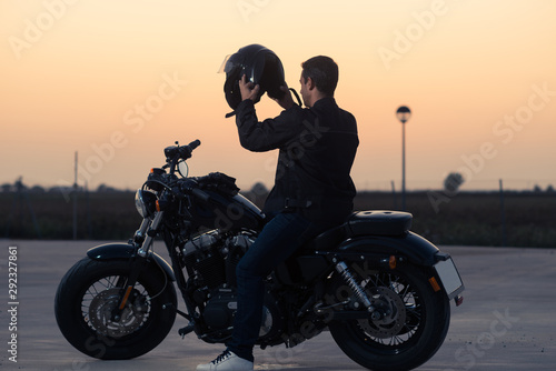 Biker man with his custom motorcycle putting on a helmet at sunset