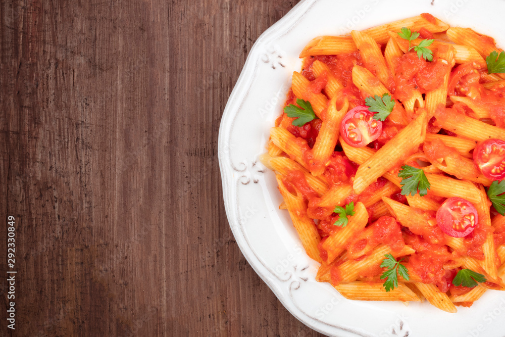 A close-up of penne pasta with tomato sauce, shot from above on a dark rustic wooden background with a place for text A close-up of penne pasta with tomato sauce, shot from above on a dark rustic wooden background with a place for text