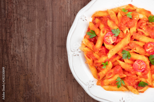 A close-up of penne pasta with tomato sauce, shot from above on a dark rustic wooden background with a place for text