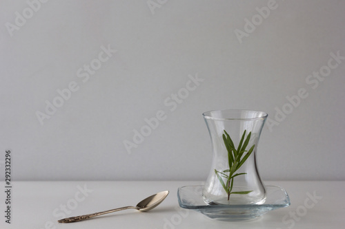 Empty Armudu tea glass with branch of rosemary in it and spoon on the table on white background photo