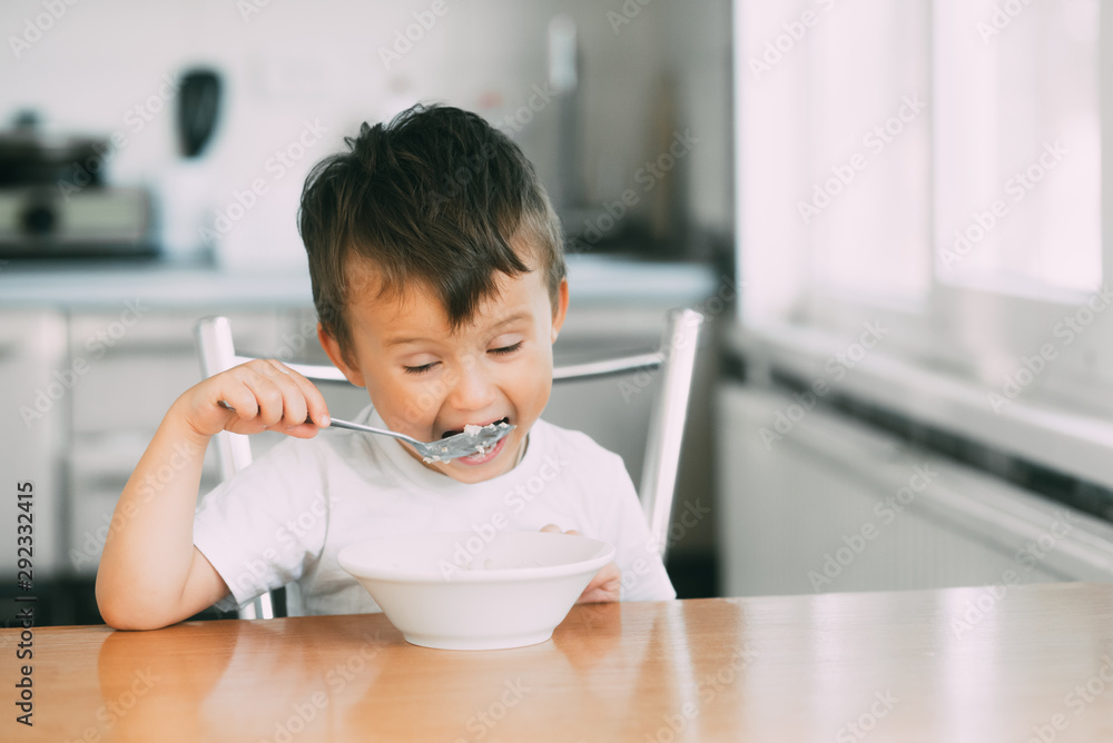 A little boy in the kitchen eating oatmeal from a white plate A little boy in the kitchen eating oatmeal from a white plate