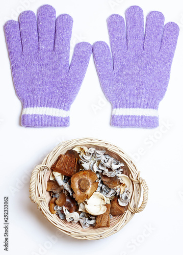 WOOL GLOVES AND BASKET OF DRY FLOWERS OF AUTUMN ON WHITE BACKGROUND. START OF THE AUTUMN COLD