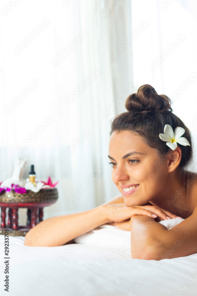 Nice relaxing young woman with flower on hair lying down on towel on bench spa. Smiling on camera. Taking massage and treatment in luxury salon in Thailand. Nice relaxing young woman with flower on hair lying down on towel on bench spa. Smiling on camera. Taking massage and treatment in luxury salon in Thailand.