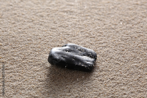 little black stone on the sand with sand grais falling on and copy space for your text photo