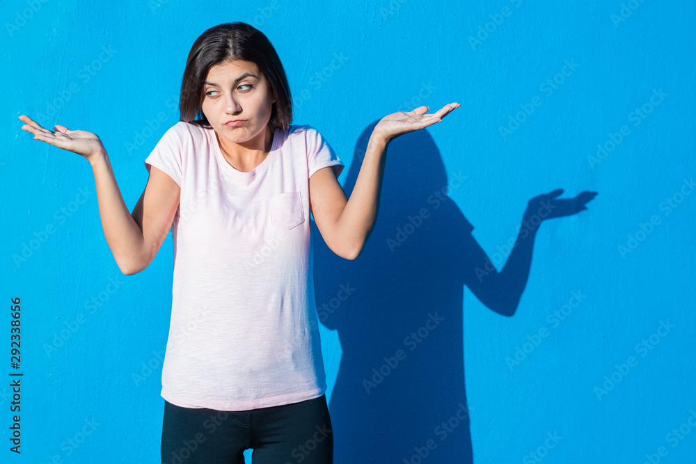 Beautiful cheerful young girl wearing casual clothes standing isolated over blue background on a sunny day. Woman does not know and asking questions. People and emotions image concept with copy space. Beautiful cheerful young girl wearing casual clothes standing isolated over blue background on a sunny day. Woman does not know and asking questions. People and emotions image concept with copy space.
