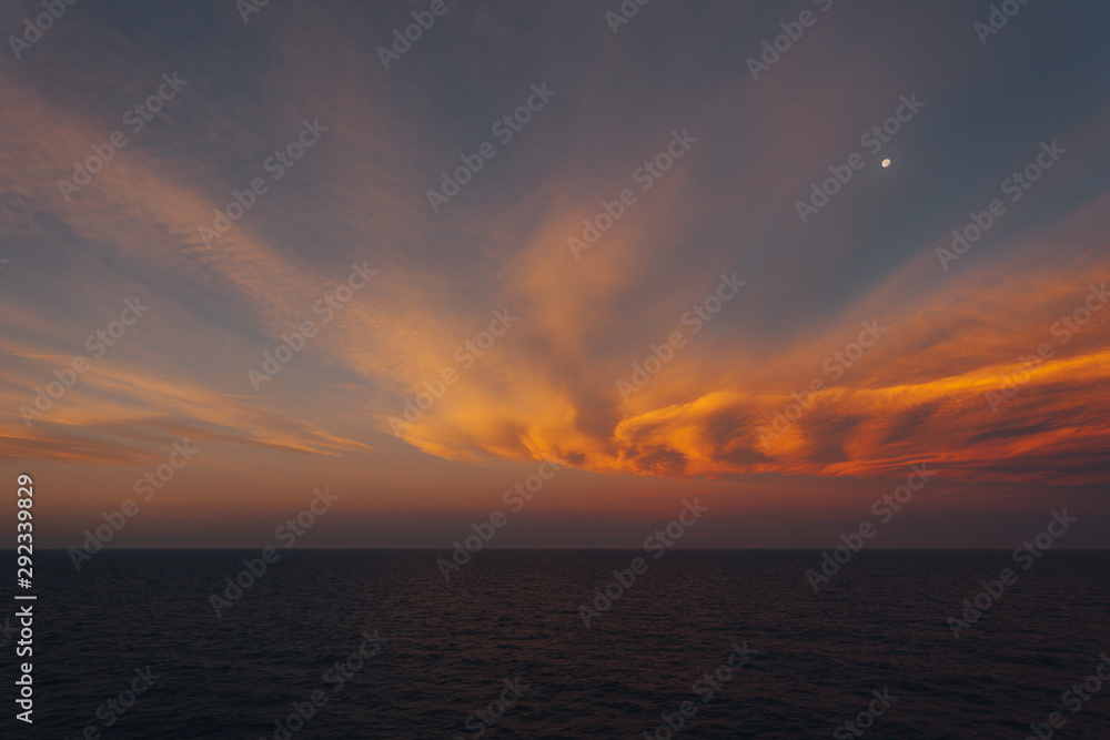 Moon rising over the sea and dreamy orange-colored clouds after sunset