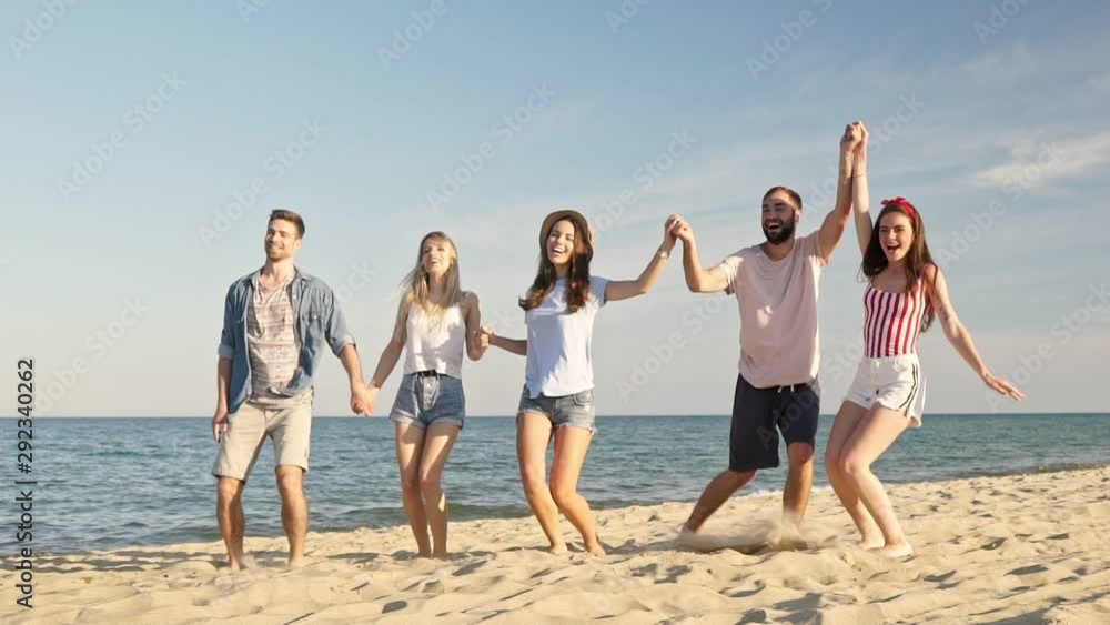 Group of young cheerful friends smiling and jumping together while having fun on the beach near the sea Group of young cheerful friends smiling and jumping together while having fun on the beach near the sea