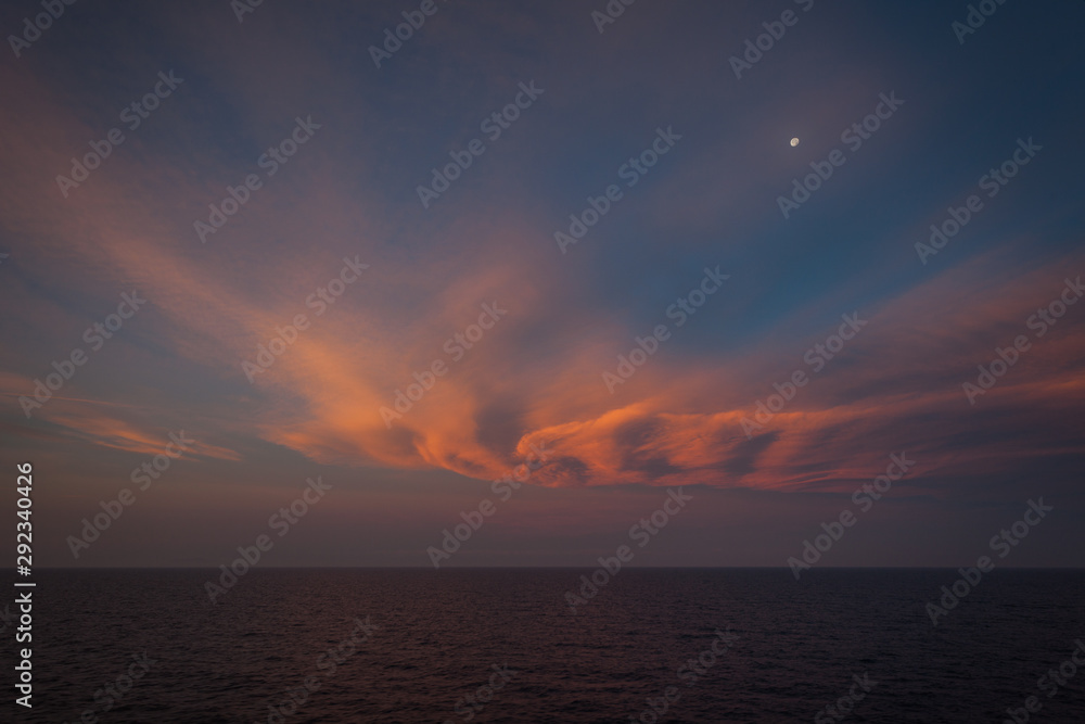 Moon rising over the sea and orange-colored clouds after sunset