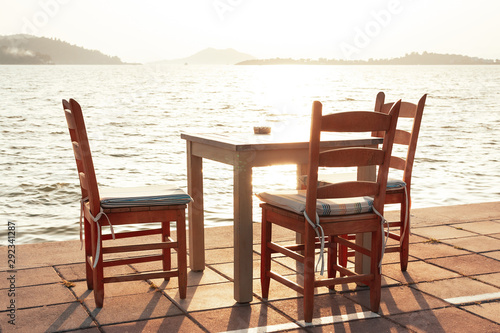 Beach cafe with sea view at sunset, empty table, three chairs, vacant for guests. Simple, authentic wooden furniture. Beautiful summer holiday concept. Horizon with misty mountains on distant island