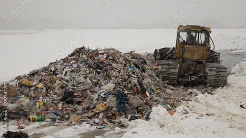 Garbage dump in the snow. Bulldozer rakes a bunch of garbage.