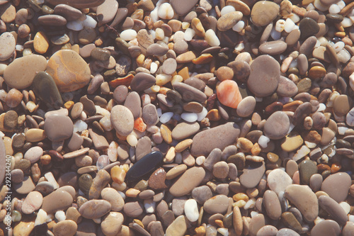 Wet glossy multi-colored pebble stones on the beach. Soft pink smoky texture for marine summer vacation background design.