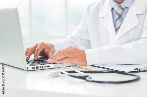 Senior doctor at his office in hospital working close-up using laptop typing
