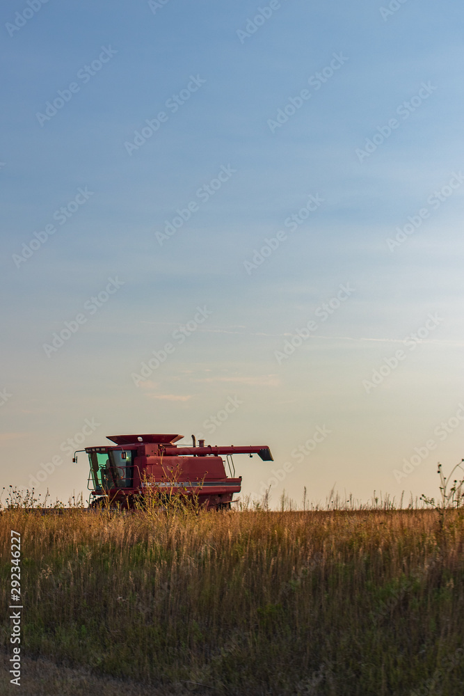 Fototapeta premium Older Red Combine in Field as Sun Sets