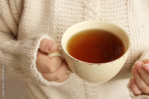 cup of hot fragrant tea in the hands of a woman, texture of a knitted sweater, close-up, copy space, concept of winter or autumn mood
