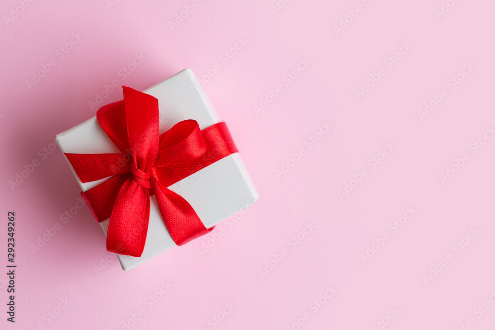 White box with a red ribbon on a light pink background, copy space. Greeting card concept. Gift concept White box with a red ribbon on a light pink background, copy space. Greeting card concept. Gift concept