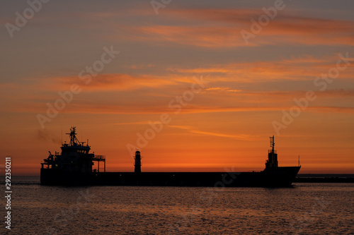 Silhouette of a big container ship at sunrise and exit from a harbor