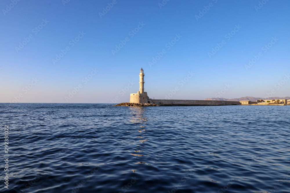 Lighthouse in Chania on a sunny day with blue sky and reflection on water.