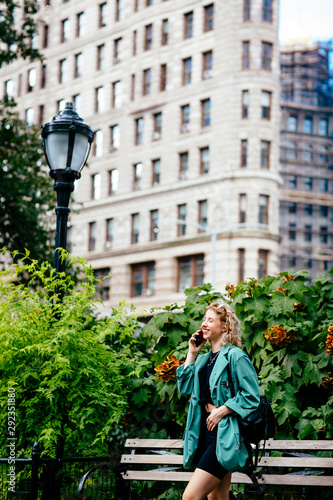 Happy woman talking on phone in a city park with buildings, New York City