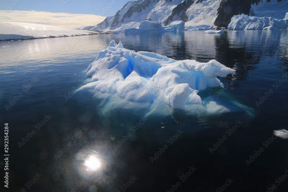 wystający ponad taflę wody wierzchołek góry lodowej przy wybrzeżu antarktydy w słoneczny dzień - obrazy, fototapety, plakaty 