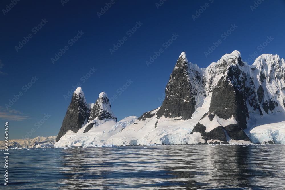 skaliste i ośnieżone wybrzeże antarktydy w słoneczny dzień - obrazy, fototapety, plakaty 