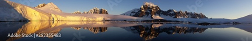 panorama ośnieżone skalne wybrzeże antarktydy odbijające się w gładkiej tafli wody o zachodzie słońca