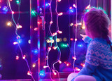 Happy little cute, beautiful girl 5 years old is sitting on the window and playing with Christmas lights and  Christmas decoration. Dark-blue theme. 