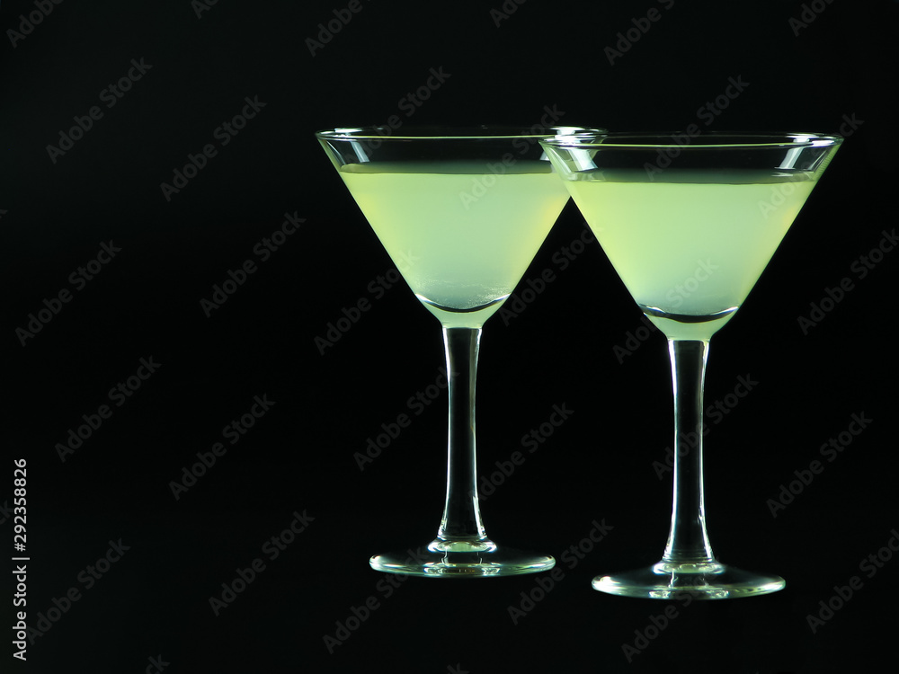 A classic daiquiri alcoholic cocktail of light green color from white rum, simple syrup and lime juice, in two conical cocktail glasses on a dark background A classic daiquiri alcoholic cocktail of light green color from white rum, simple syrup and lime juice, in two conical cocktail glasses on a dark background