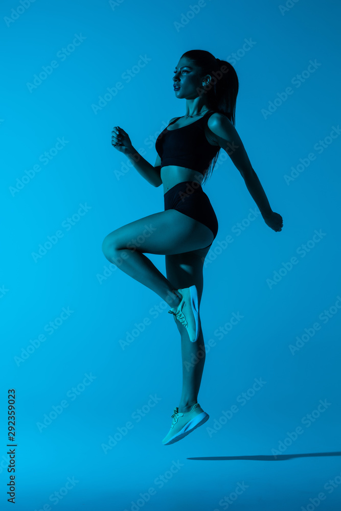 Strong young sports woman jump isolated over purple wall background.