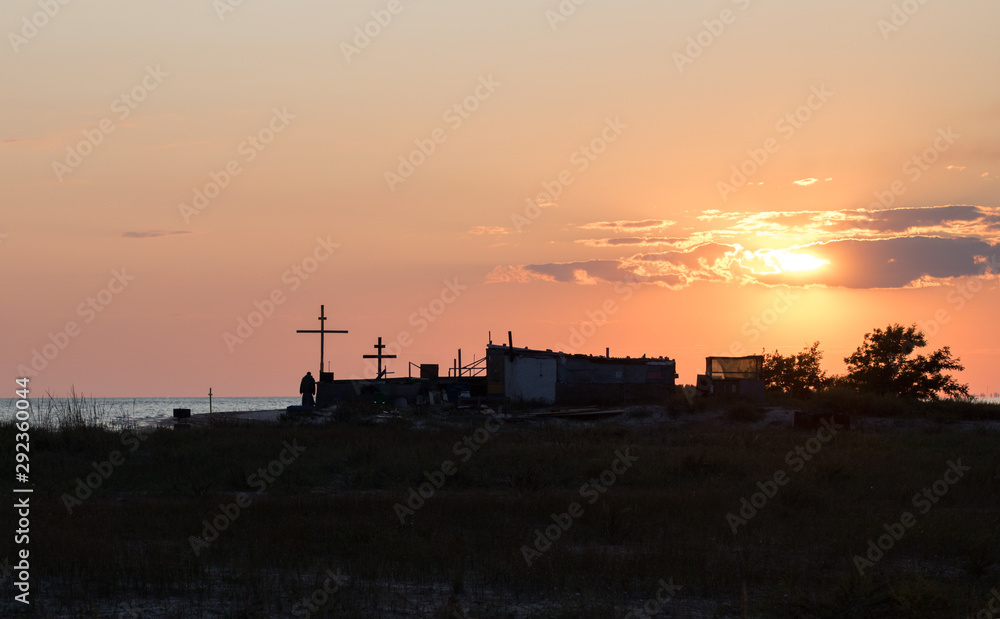 hermit monk house and crosses on the beach on the island, red sunset on the sea