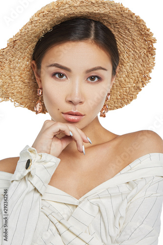 Cropped close-up shot of a young Asian girl in a straw hat and white striped shirt wearing stud earrings with pink drop-shaped pendants made of gems similar to tourmalin. photo