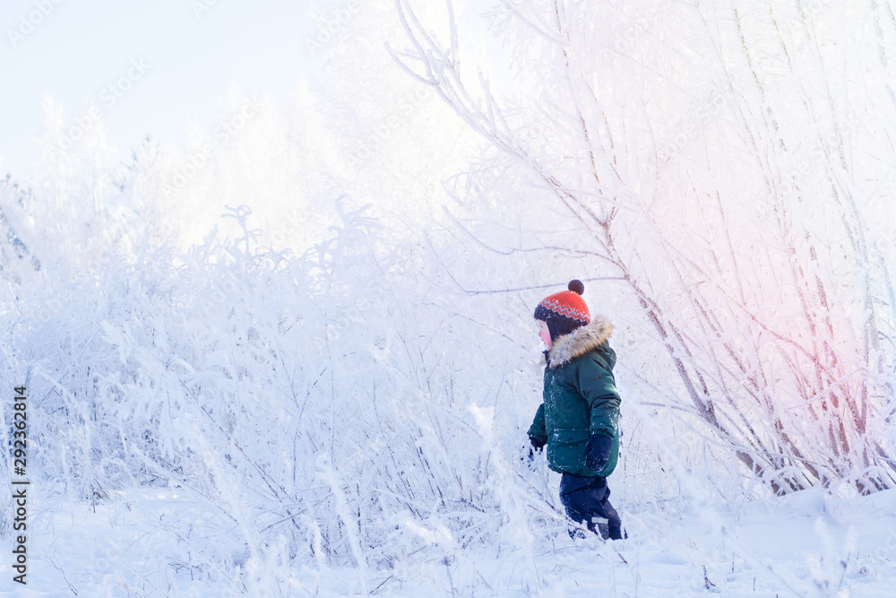 A boy in a bright orange hat walks through the snowy winter Park