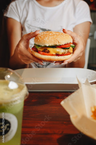 tasty burger. stylish hipster woman holding juicy hamburger in hands close up. boho girl with hamburger at cafe food festival.