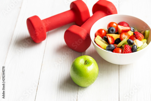 Healthy lifestyle for women diet with fresh fruits salad and dumbbells sport equipment, fruit healthy green apples on wooden. Healthy Concept.