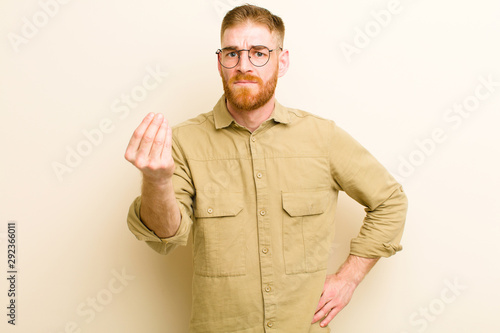 young red head man making capice or money gesture, telling you to pay your debts! against beige background photo