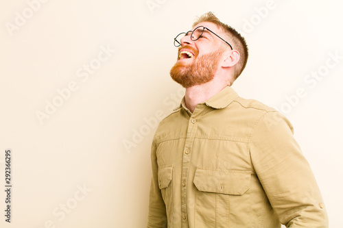 young red head man screaming furiously, shouting aggressively, looking stressed and angry against beige background photo