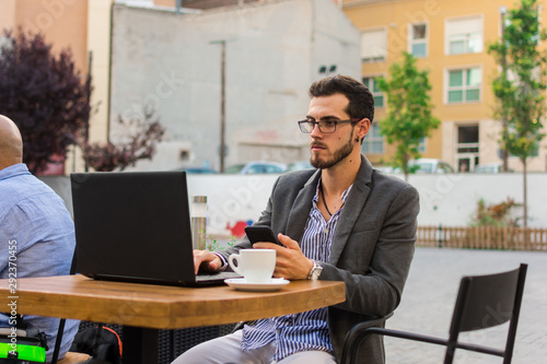 Young businessman is working in a bar terrace with his laptop and smartphone